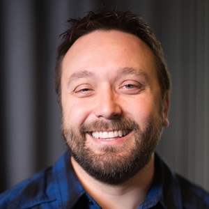 portrait of a man with a beard smiling and wearing a blue shirt